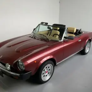 Fiat 124 Spider Cabriolet in Bordeauxrot, spätes Modell, Innenraum mit beigen Sitzen, präsentiert im Ausstellungsraum.