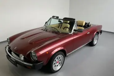 Fiat 124 Spider Cabriolet in Bordeauxrot, spätes Modell, Innenraum mit beigen Sitzen, präsentiert im Ausstellungsraum.