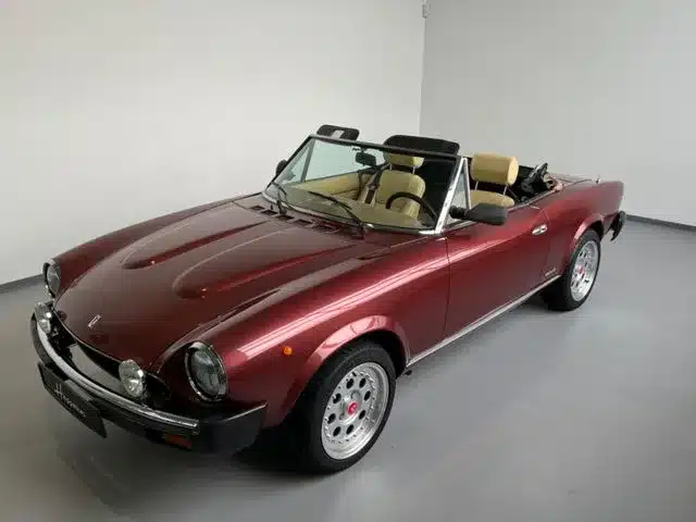 Fiat 124 Spider Cabriolet in Bordeauxrot, spätes Modell, Innenraum mit beigen Sitzen, präsentiert im Ausstellungsraum.