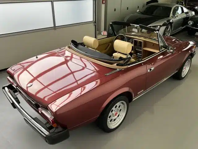 Roter Fiat 124 Spider Cabrio, Baujahr späte Serie, mit beigen Ledersitzen, steht in einer hellen Garage