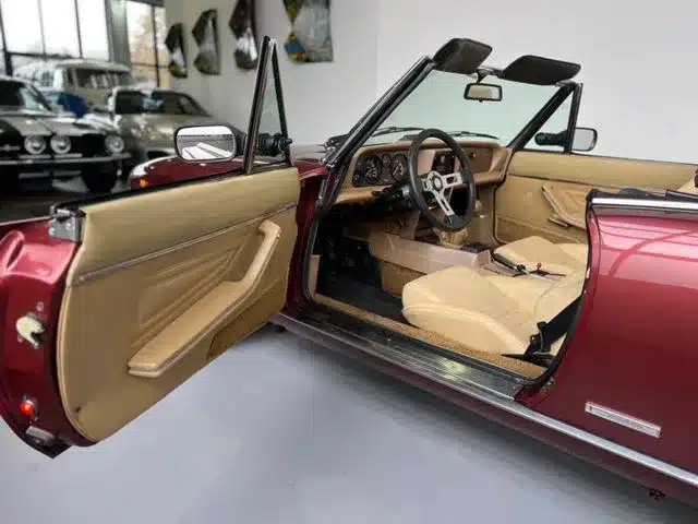 Innenraum und Cockpit eines offenen Fiat 124 Spider mit beigen Sitzen, geöffneten Türen und roter Karosserie