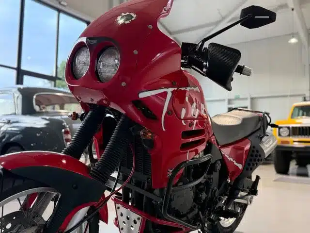 Rote Triumph T900 Tiger Reiseenduro mit Doppelscheinwerfern und markanter Silhouette in einer hellen Garage.