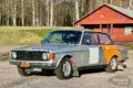 Volvo 142 von 1970 als Rallyefahrzeug mit grau-oranger Lackierung und Überrollkäfig auf einem Parkplatz
