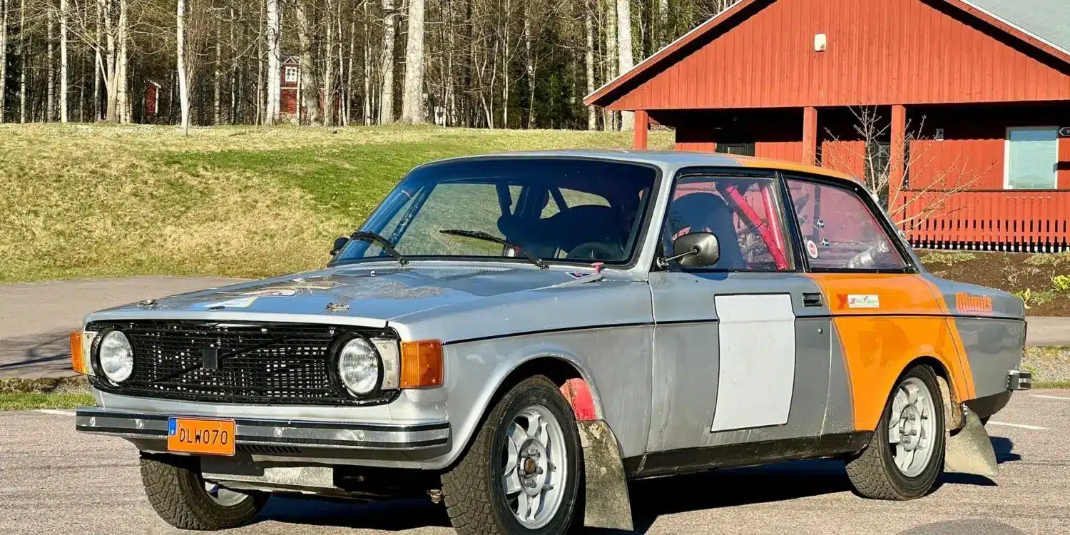 Volvo 142 von 1970 als Rallyefahrzeug mit grau-oranger Lackierung und Überrollkäfig auf einem Parkplatz