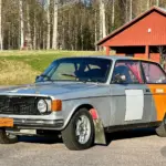 Volvo 142 von 1970 als Rallyefahrzeug mit grau-oranger Lackierung und Überrollkäfig auf einem Parkplatz