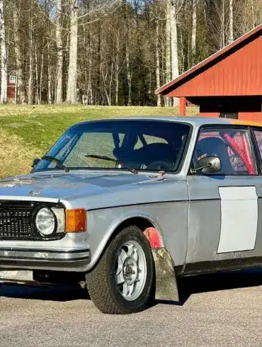 Volvo 142 von 1970 als Rallyefahrzeug mit grau-oranger Lackierung und Überrollkäfig auf einem Parkplatz