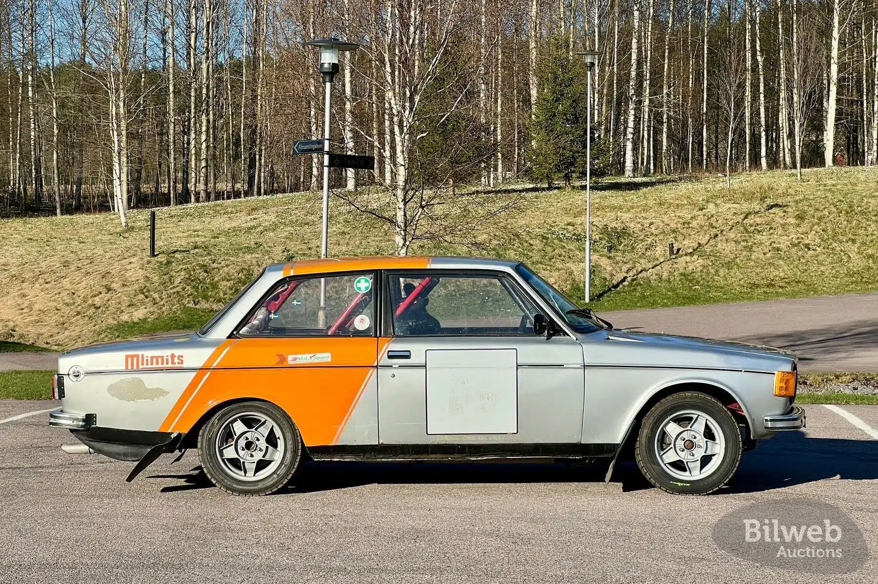 Seitenansicht eines Volvo 142 Rallyeautos Baujahr 1970 mit orange-grauer Lackierung und sportlichen Modifikationen, geparkt im Freien.