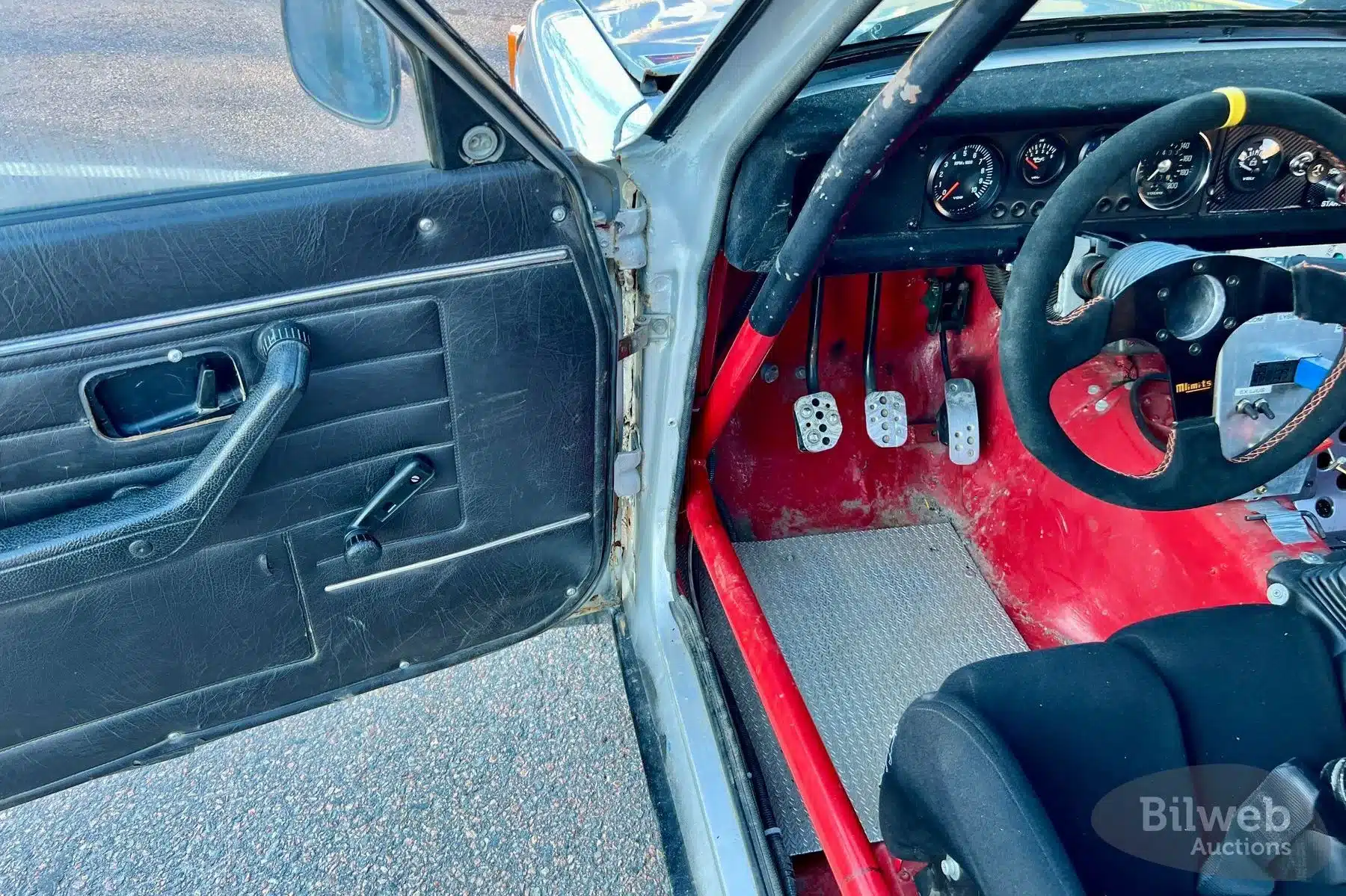 Blick in den spartanischen Innenraum eines Volvo 142 Rallyeautos mit Überrollkäfig, Alupedalen und Rennlenkrad.