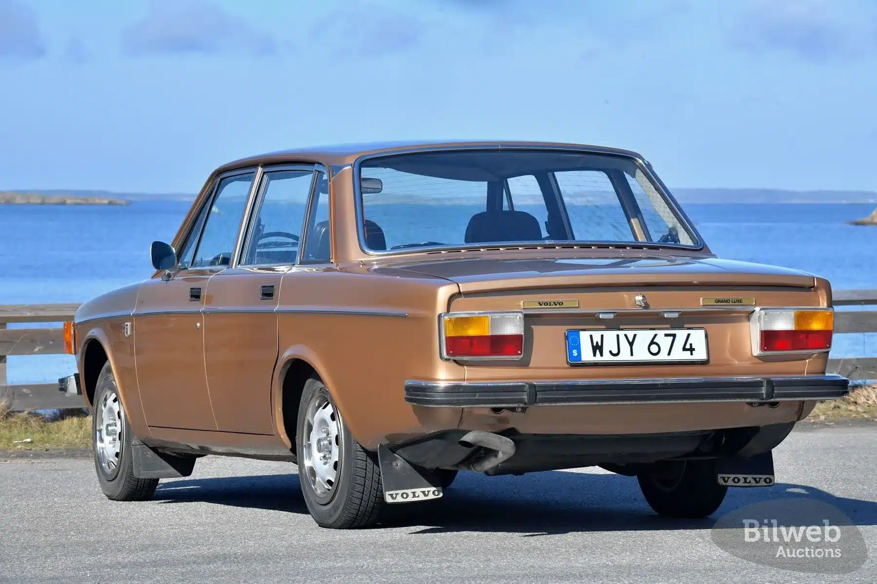 Brauner Volvo 144 GL B20 von 1973, Heckansicht, vor blauem Wasser und Himmel.