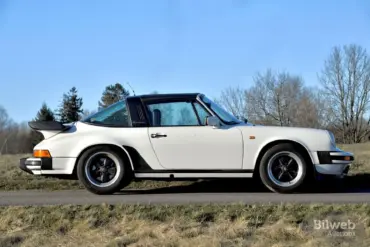 Weißer Porsche 911 SC Targa 3,0, Baujahr 1981, seitlich fotografiert, mit schwarzem Targa-Bügel und Fuchs-Felgen auf einer Landstraße vor natürlicher Kulisse.