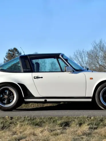 Weißer Porsche 911 SC Targa 3,0, Baujahr 1981, seitlich fotografiert, mit schwarzem Targa-Bügel und Fuchs-Felgen auf einer Landstraße vor natürlicher Kulisse.