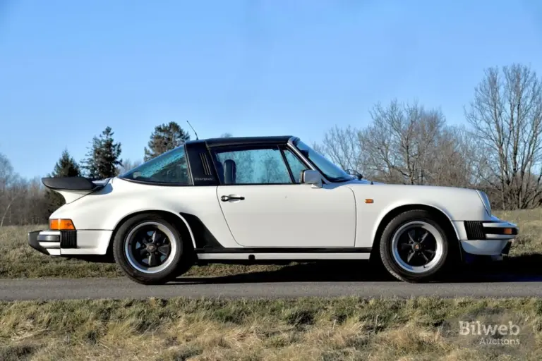 Weißer Porsche 911 SC Targa 3,0, Baujahr 1981, seitlich fotografiert, mit schwarzem Targa-Bügel und Fuchs-Felgen auf einer Landstraße vor natürlicher Kulisse.