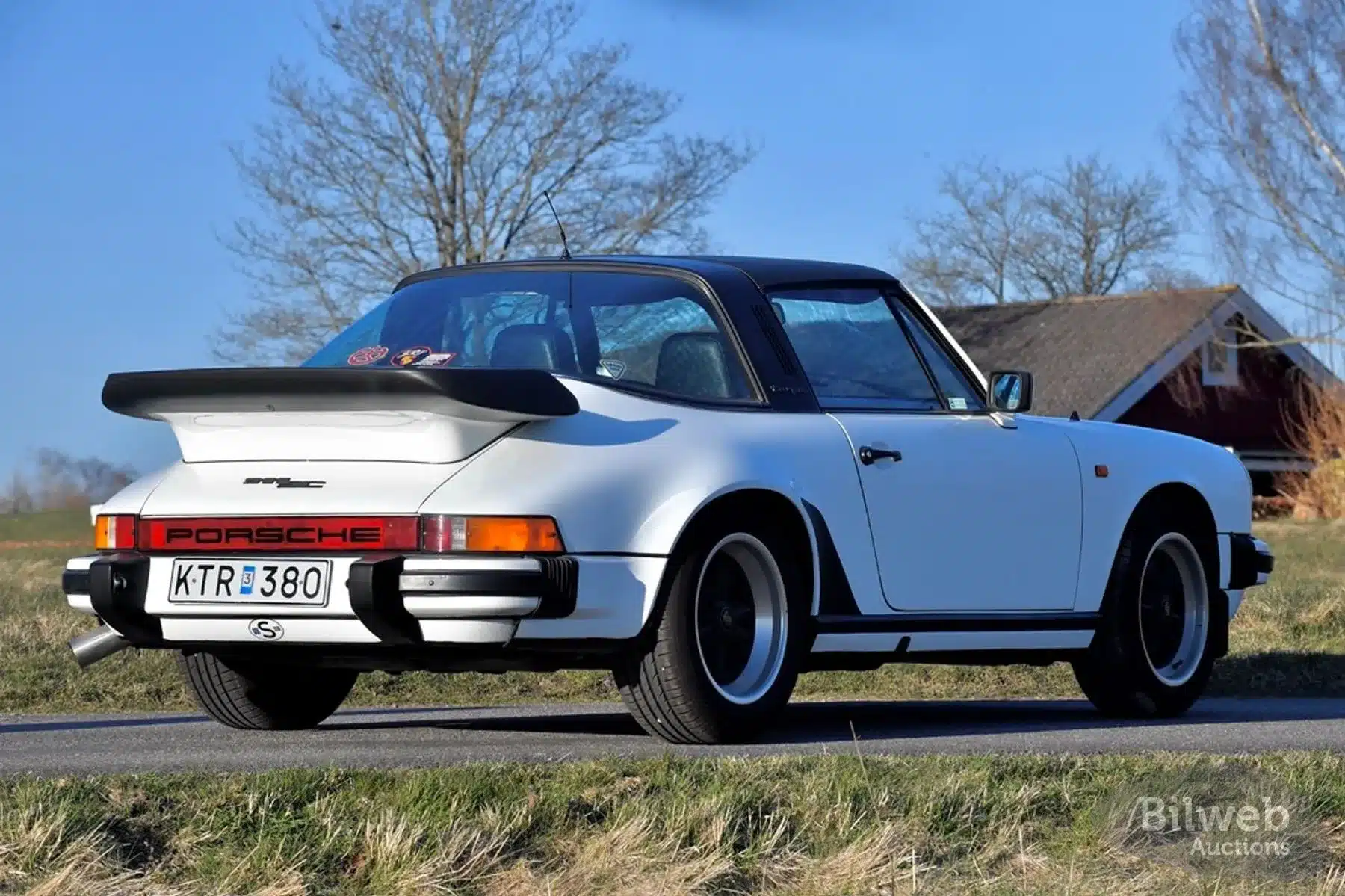 Weißer Porsche 911 SC Targa 3,0 Baujahr 1981 von hinten, mit markantem Heckspoiler und Targa-Dach auf einer Landstraße.