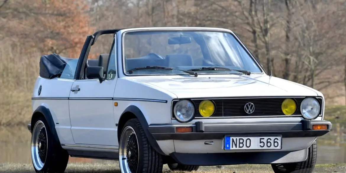 Weißes VW Golf Mk I Cabriolet von 1986 mit geöffnetem Verdeck und zeitgenössischer Patina, aufgenommen im Freien