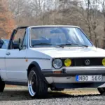 Weißes VW Golf Mk I Cabriolet von 1986 mit geöffnetem Verdeck und zeitgenössischer Patina, aufgenommen im Freien