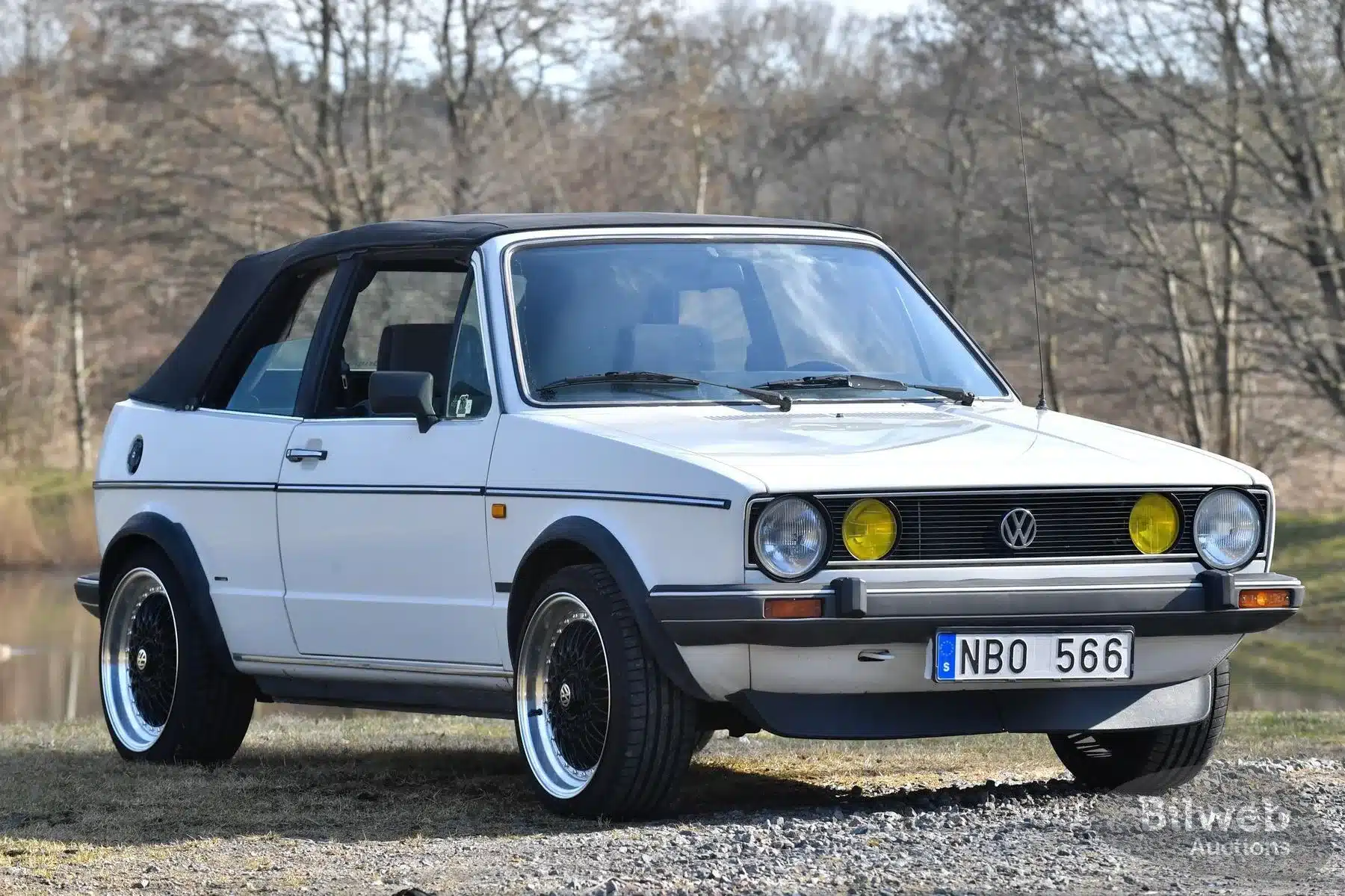 Ein weißer VW Golf Mk I Cabriolet von 1986 mit schwarzem Verdeck und gelben Zusatzscheinwerfern, seitliche Frontansicht, aufgenommen im Freien.