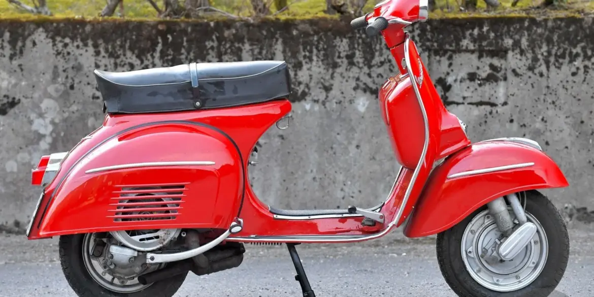 Seitenansicht einer restaurierten roten Piaggio Vespa 180 Super Sport von 1966 vor einer Steinmauer.