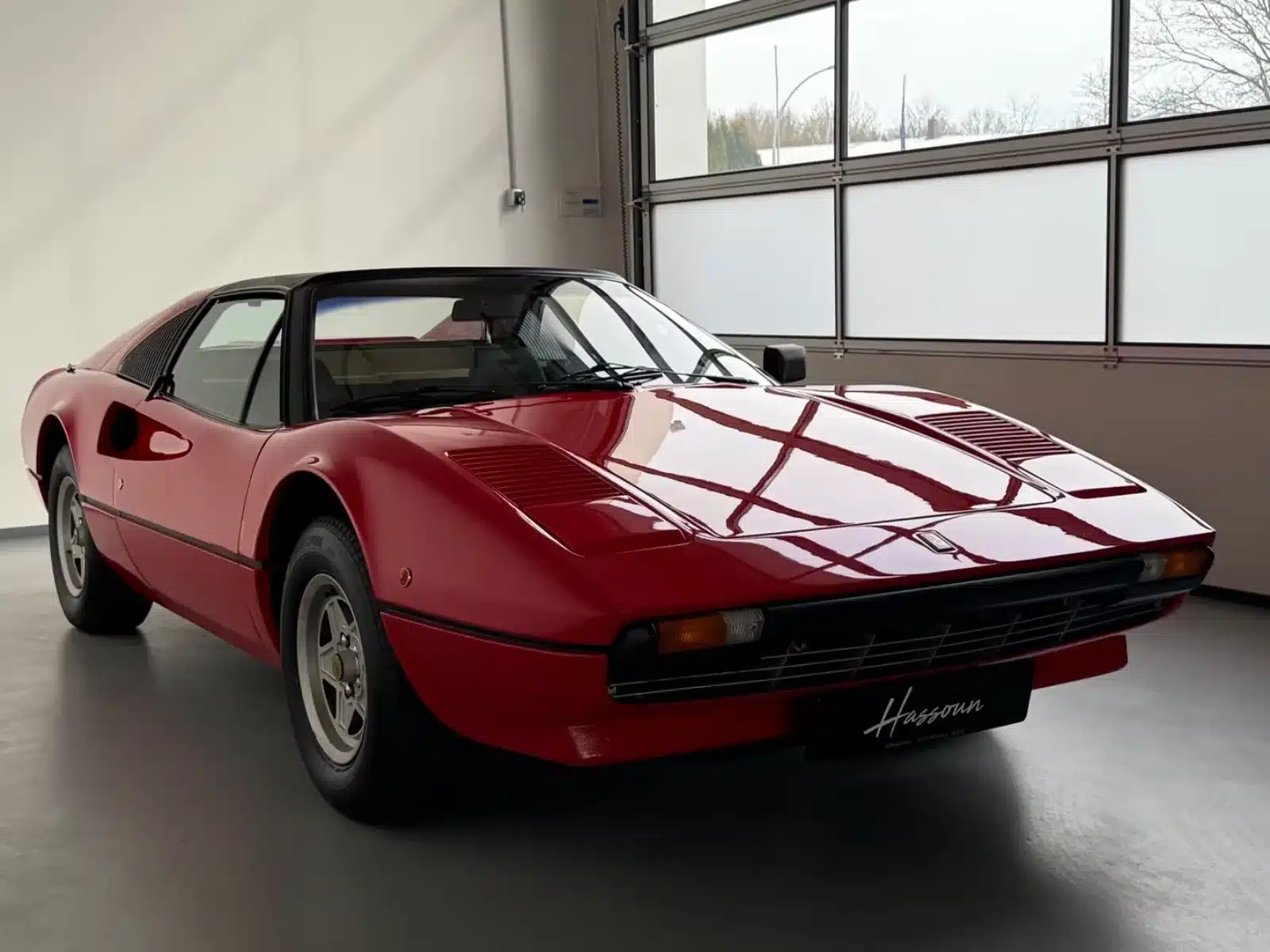 Roter Ferrari 308 GTSi mit Targa-Dach, Seitenansicht von vorne, in einer hellen Halle abgestellt.