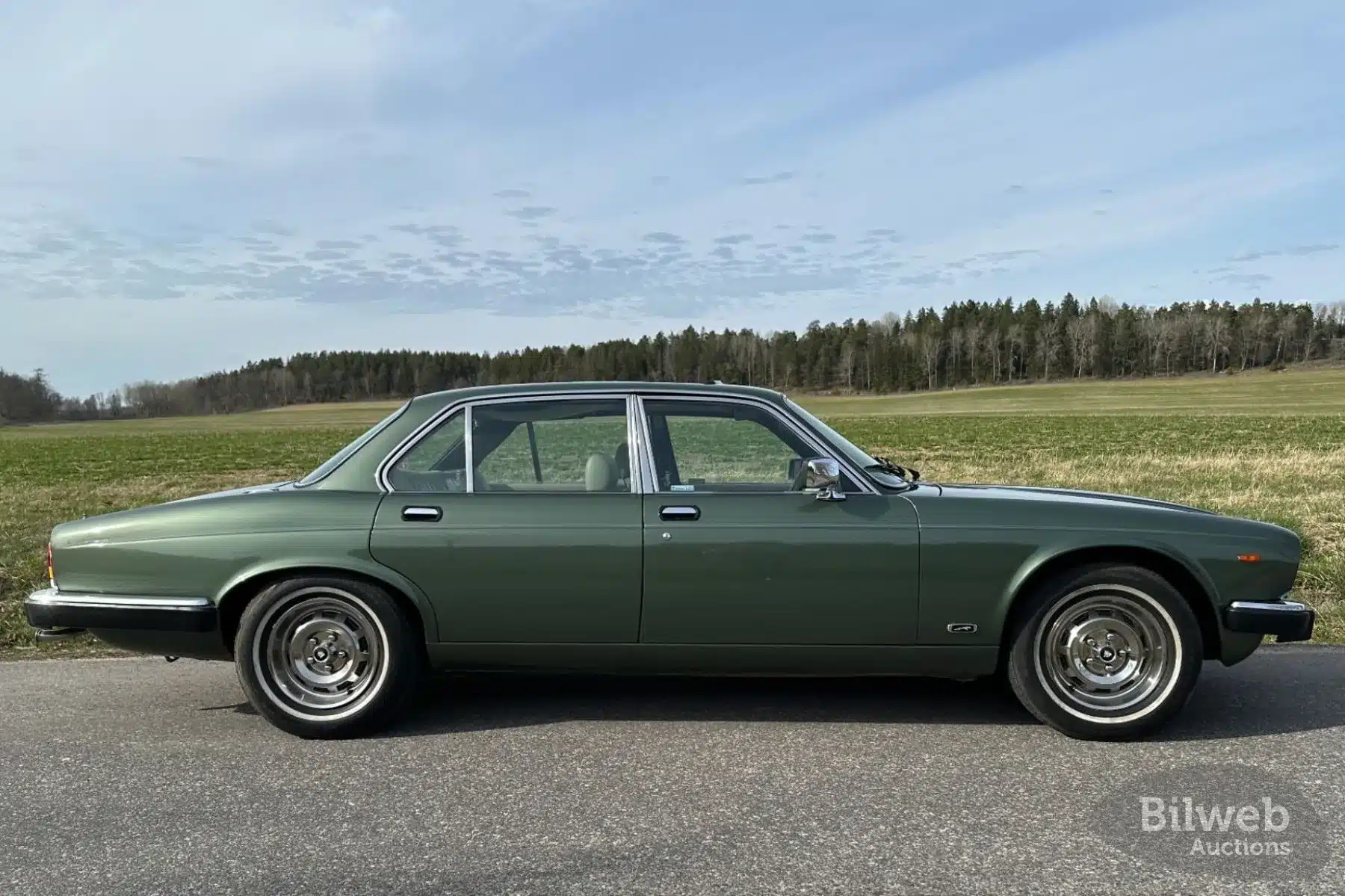 Grüner Jaguar XJ6 Series III von 1985, Seitenansicht, auf Asphalt vor Waldhintergrund