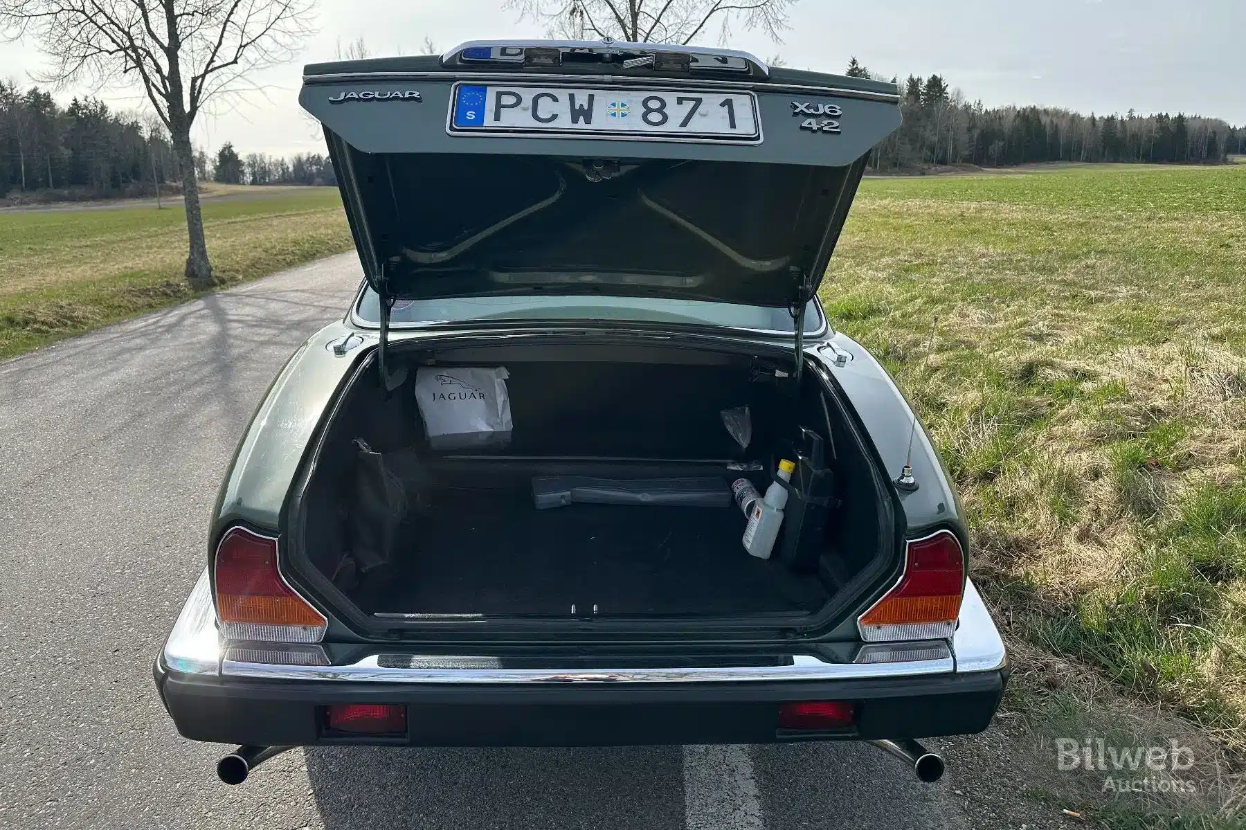 Der geöffnete Kofferraum eines Jaguar XJ6 4.2L Series III Baujahr 1985, fotografiert von hinten auf einer ländlichen Straße.