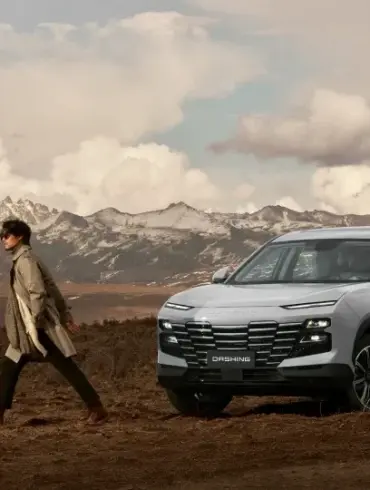 Jetour Dashing SUV steht vor einer Bergkulisse auf unbefestigtem Untergrund, Person läuft neben dem Fahrzeug.