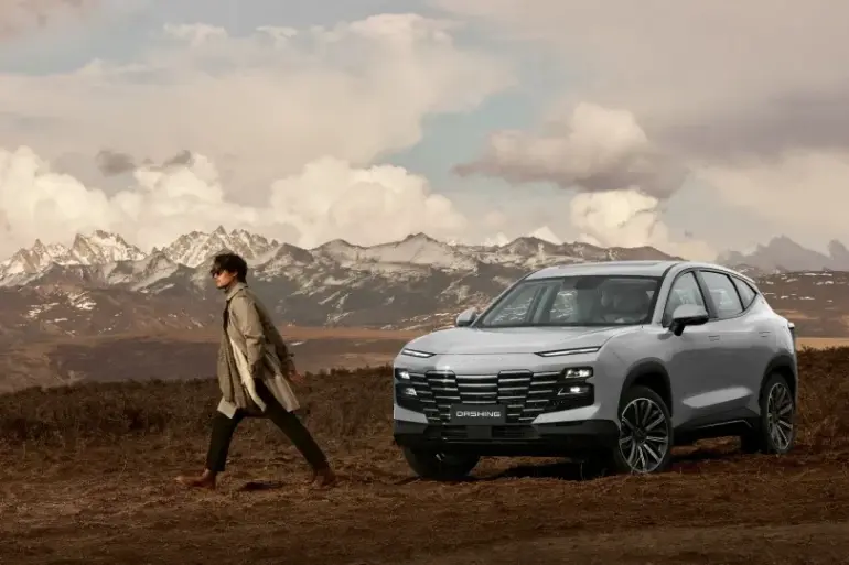 Jetour Dashing SUV steht vor einer Bergkulisse auf unbefestigtem Untergrund, Person läuft neben dem Fahrzeug.