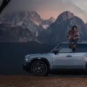 JETOUR T2 i-DM SUV mit Panoramadach, Mann mit Hund auf dem Dach, Berge im Hintergrund bei Sonnenuntergang.