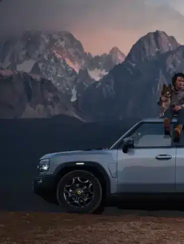 JETOUR T2 i-DM SUV mit Panoramadach, Mann mit Hund auf dem Dach, Berge im Hintergrund bei Sonnenuntergang.