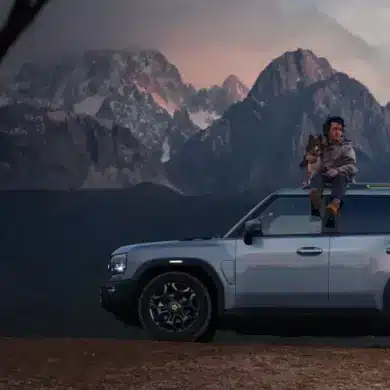 JETOUR T2 i-DM SUV mit Panoramadach, Mann mit Hund auf dem Dach, Berge im Hintergrund bei Sonnenuntergang.