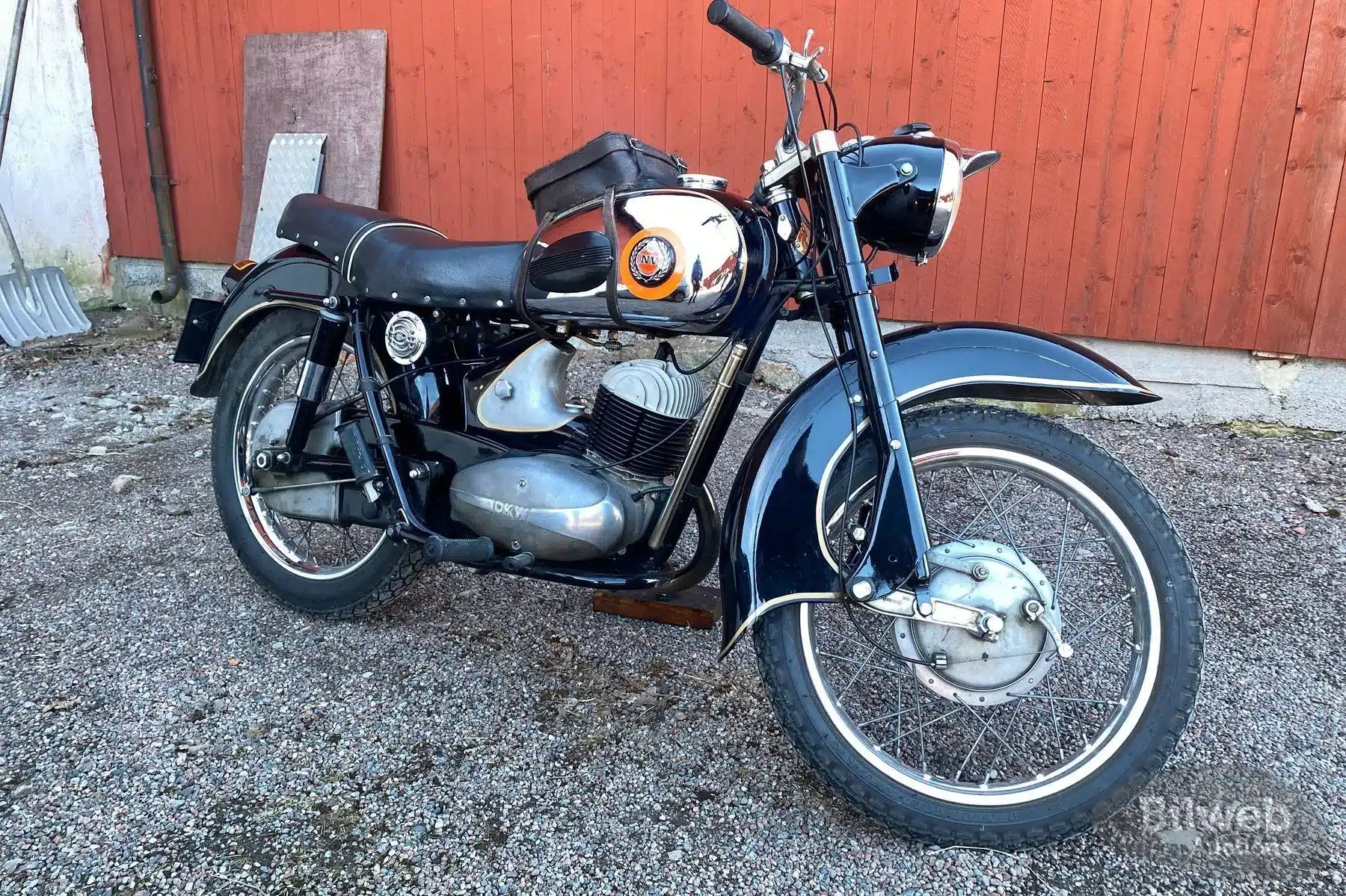 Schwarzes Oldtimer-Motorrad NV 38 von 1955 vor einer roten Holzfassade