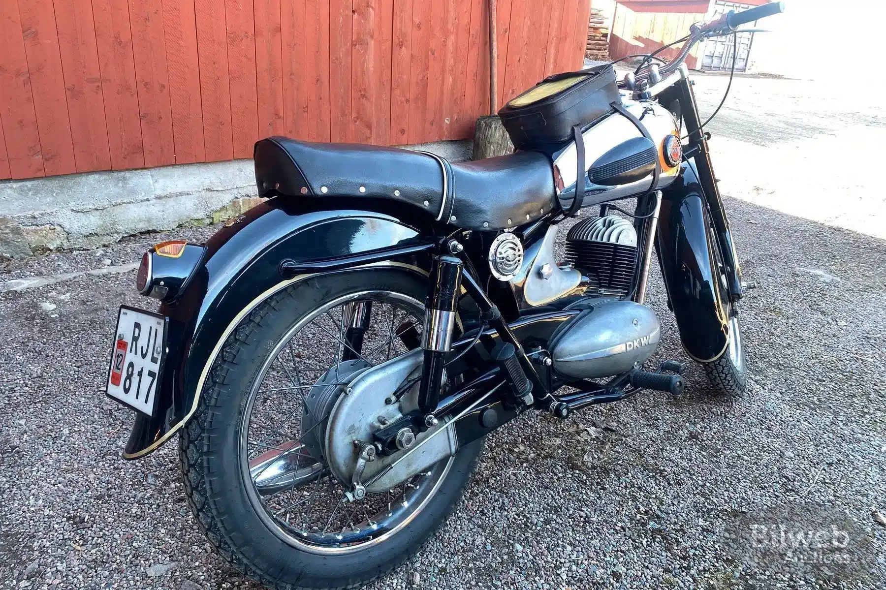 Schwarzes Motorrad NV 38 von 1955 von schräg hinten fotografiert, mit sichtbaren Gebrauchsspuren und schwedischem Nummernschild, vor einer roten Holzfassade stehend