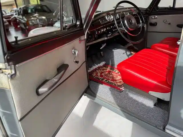 Offene Fahrertür und Innenraum eines Mercedes-Benz 180 Ponton mit roten Ledersitzen und klassischem Armaturenbrett.