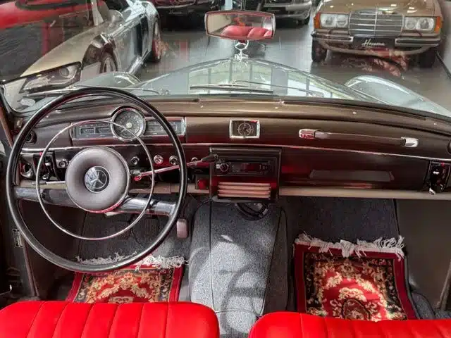 Innenansicht eines Mercedes-Benz 180 Ponton mit Blick auf Lenkrad, Armaturenbrett und rote Vordersitze.