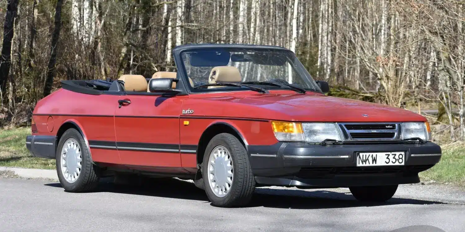 Rotes Saab 900 T16 Cabriolet 2,0 16V Turbo von 1988, offen geparkt vor Waldrand, Seitenansicht.