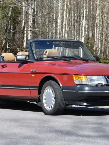 Rotes Saab 900 T16 Cabriolet 2,0 16V Turbo von 1988, offen geparkt vor Waldrand, Seitenansicht.