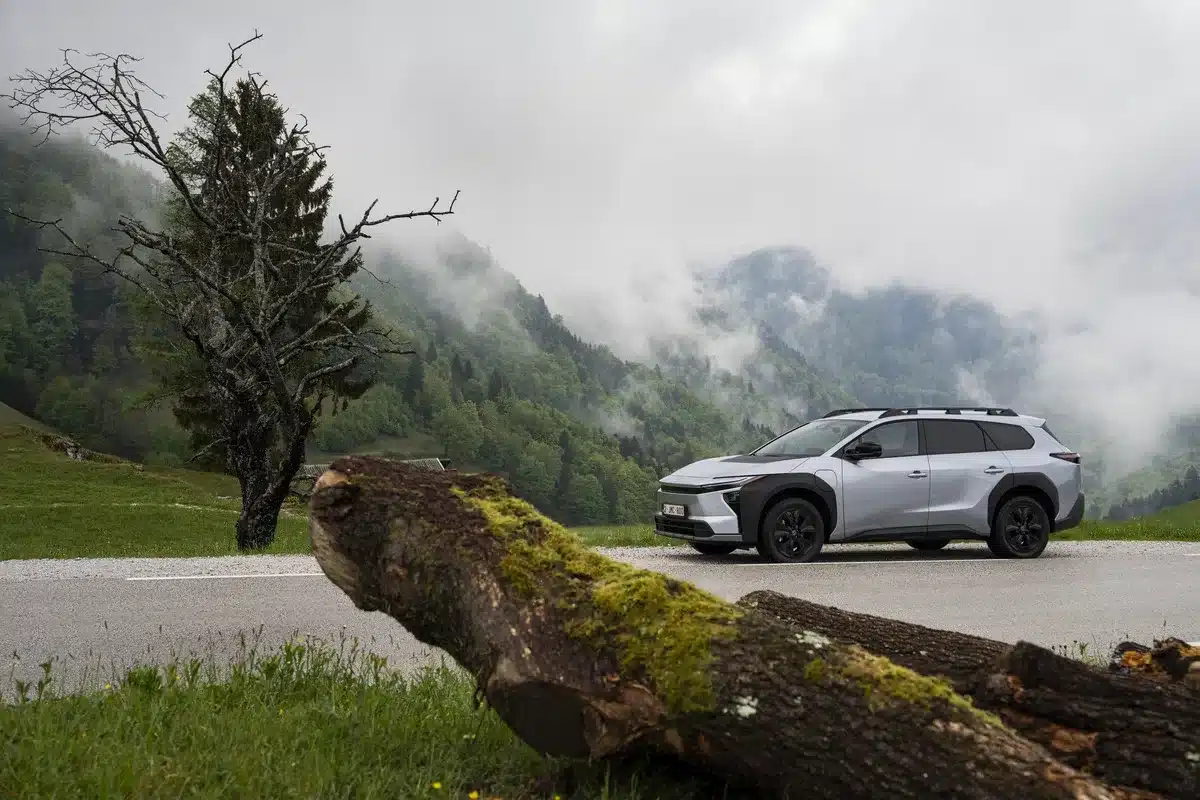 Silberner Toyota bZ4X Touring steht auf einer Straße mit einer bewaldeten Bergkulisse im Hintergrund und nebelfeuchter Atmosphäre.