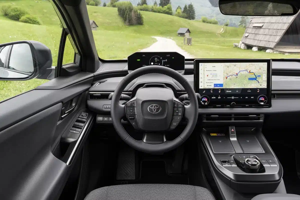 Innenraum des Toyota bZ4X Touring mit Lenkrad und großem Infotainmentsystem, Ausblick auf grüne Landschaft
