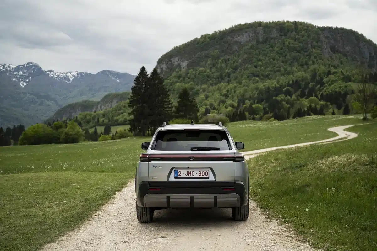 Heckansicht eines silbernen Toyota bZ4X Touring auf einem Feldweg vor grüner Hügellandschaft und Bergen.