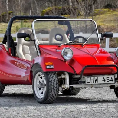 Roter Beach Buggy 1300, offener Umbau auf VW Käfer-Basis, mit weißen Speichenrädern und Überrollbügel, stehend im Freien.