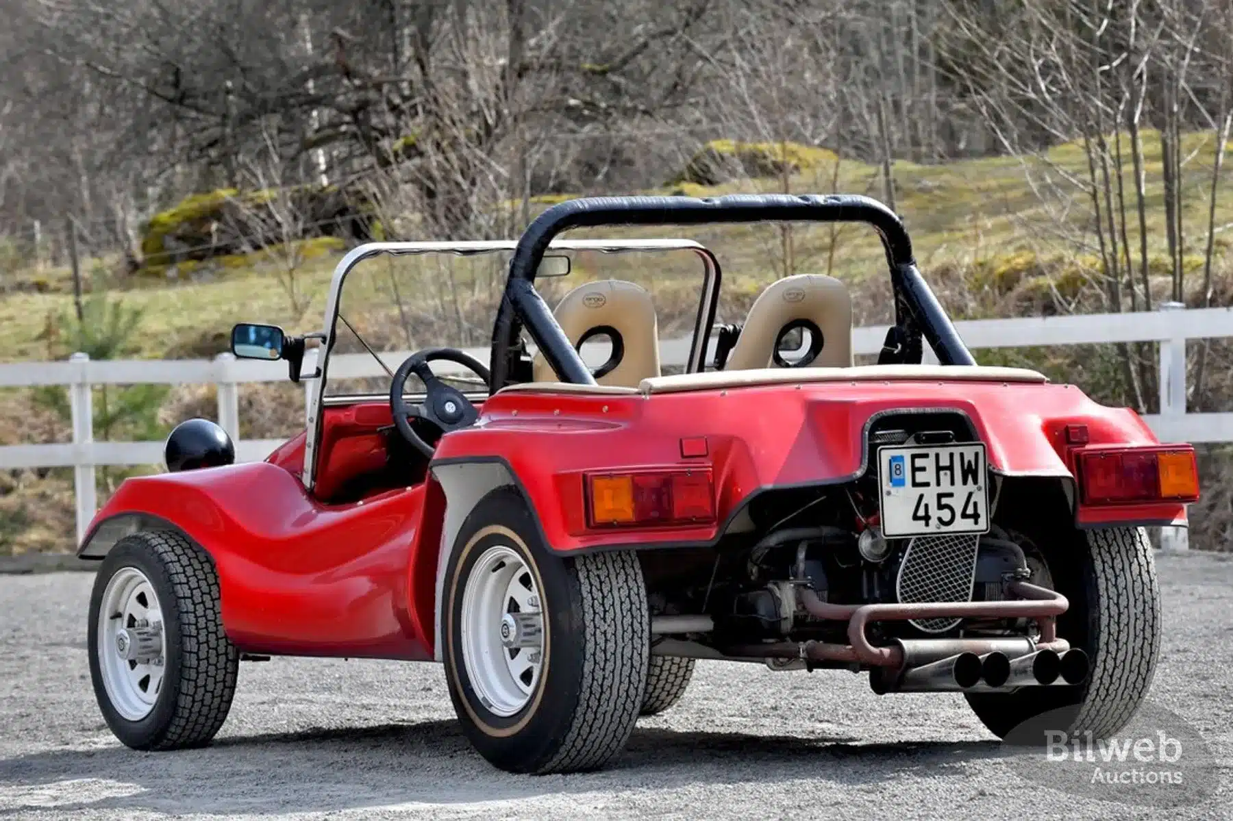Roter Beach Buggy 1300 mit weißem Überrollbügel, weißen Felgen und markanter seitlicher Auspuffanlage, Heckansicht auf einem Parkplatz im Freien.