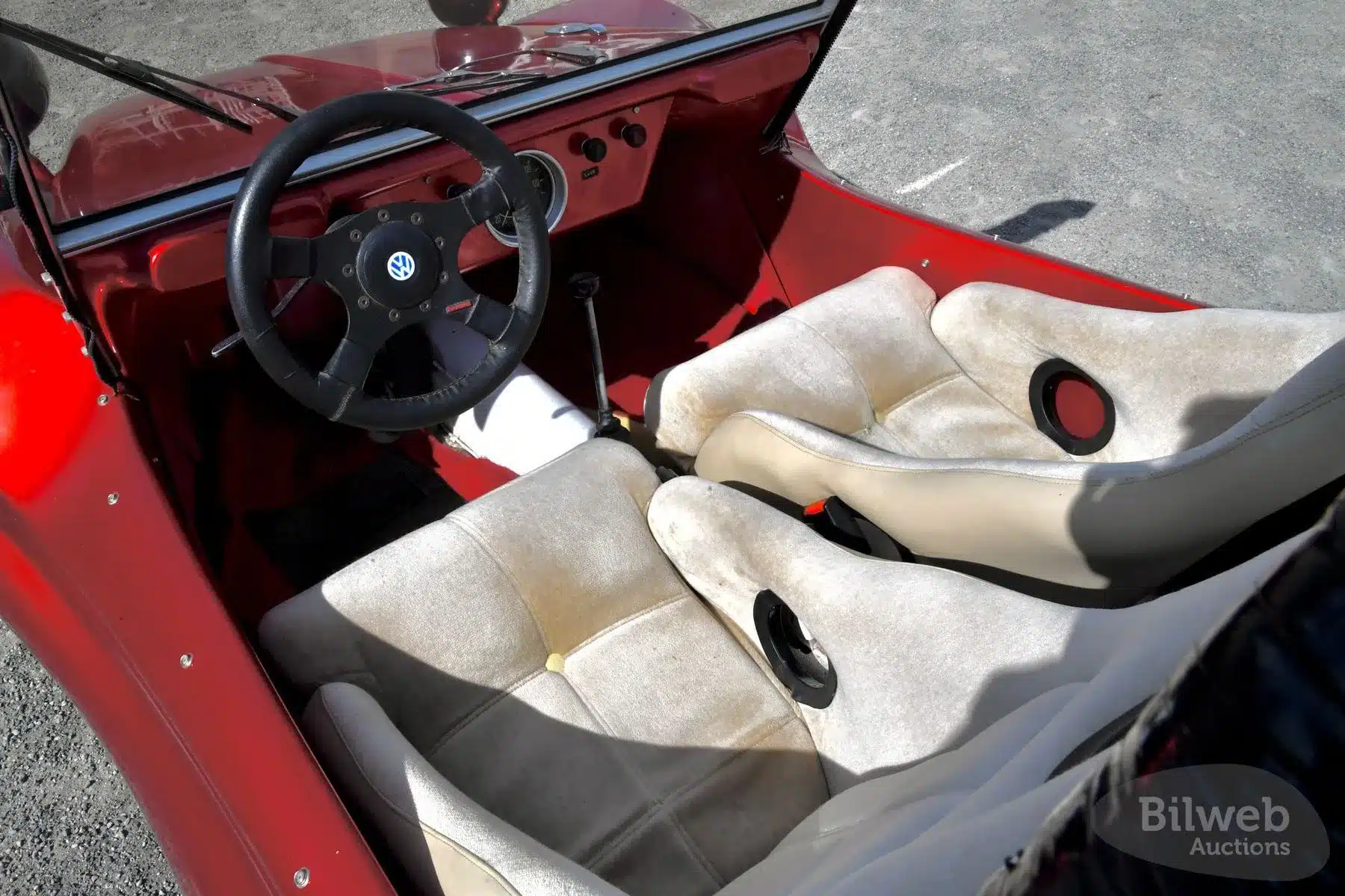 Roter Innenraum eines Beach Buggy 1300 von 1984 mit weißen Schalensitzen und VW-Sportlenkrad.