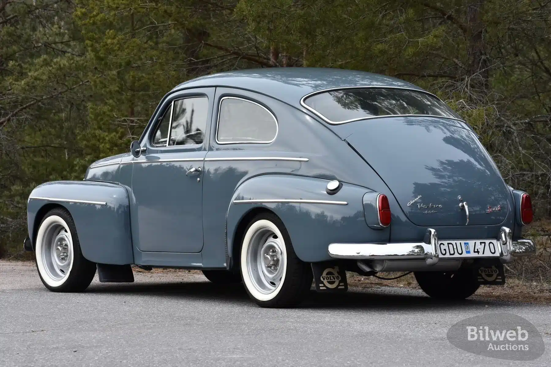 Restaurierter Volvo PV 544 B18 von 1961 in Blau aus schräger Heckansicht auf einer Landstraße, umgeben von Wald