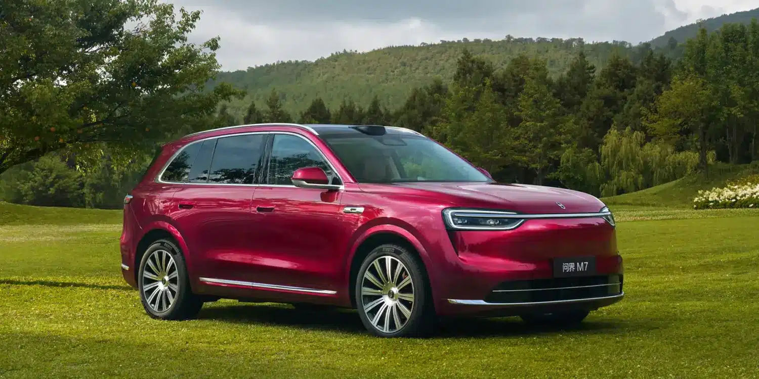 Roter Wenjie M7 SUV auf einer Wiese mit Bäumen und Bergen im Hintergrund.