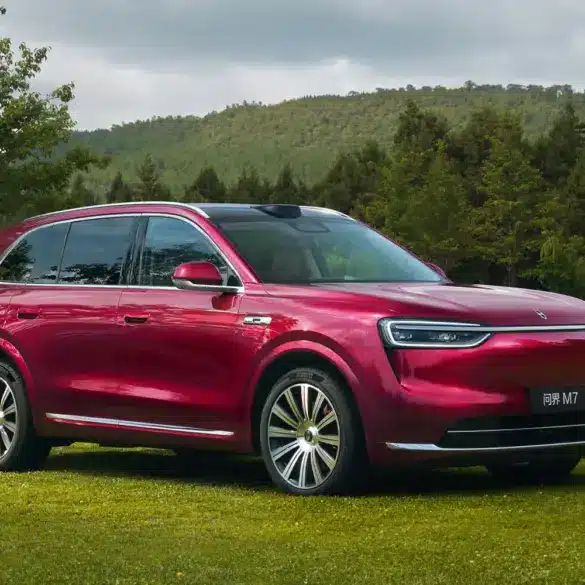Roter Wenjie M7 SUV auf einer Wiese mit Bäumen und Bergen im Hintergrund.