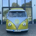 Frontalansicht eines gelb-grauen VW T1 Bulli, restauriert und elektrisch umgebaut, vor einem Autohaus