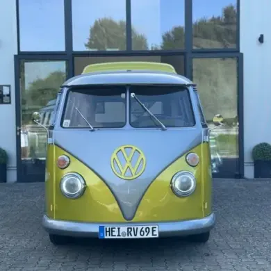 Frontalansicht eines gelb-grauen VW T1 Bulli, restauriert und elektrisch umgebaut, vor einem Autohaus