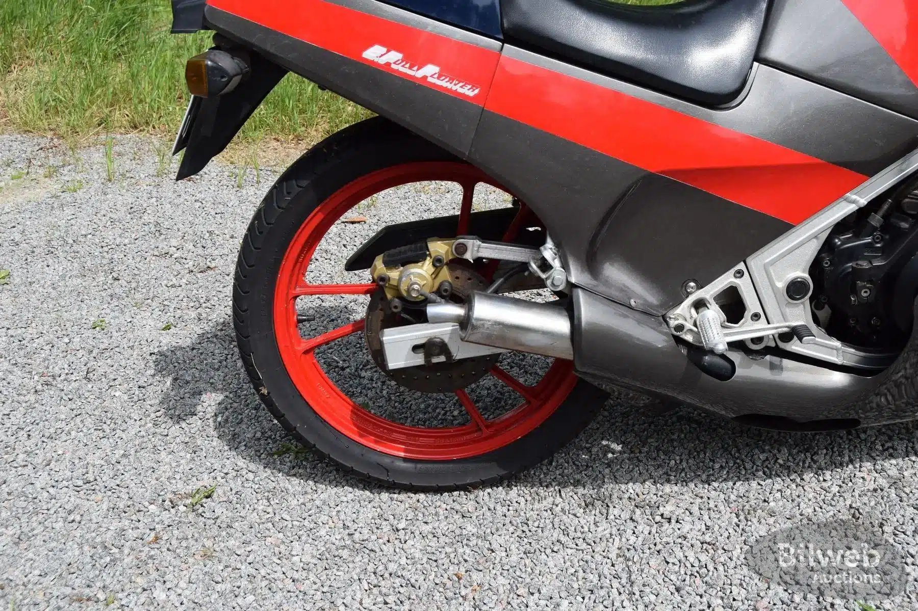 Nahaufnahme vom roten Hinterrad und Auspuff einer Suzuki RG 250 Gamma (Baujahr 1989) auf Kiesboden.