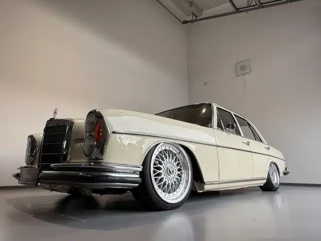 Beiger Mercedes-Benz 250 SE W108 mit Airride-Fahrwerk und BBS-Leichtmetallrädern in heller Halle, niedrige Fahrzeughöhe, klassische Limousinenform.