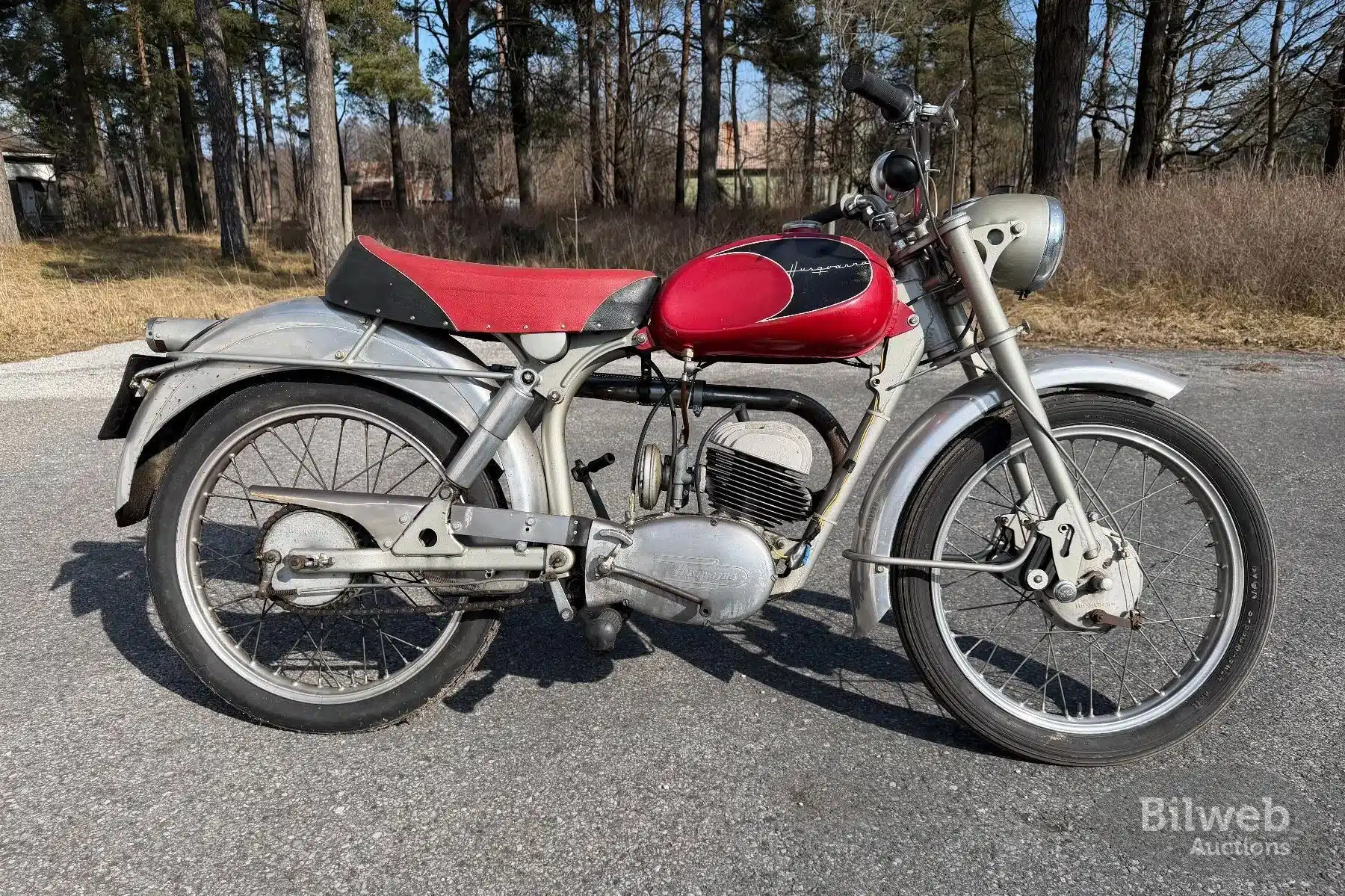 Seitenansicht einer Husqvarna 282 E Silverpil von 1960 mit rotem Tank, klassischem Design und Patina auf den Metallteilen, stehend im Freien.