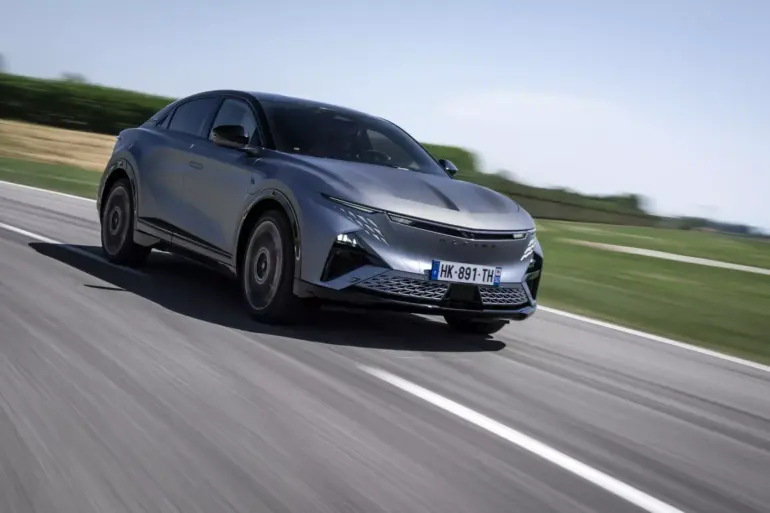 Die Alpine A390 GTS in grau fährt dynamisch auf einer Landstraße, aufgenommen bei Tageslicht.